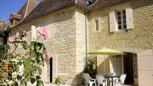 A stone building with a patio area featuring a table and chairs, and a green umbrella. - Apartment n°2 (T3) two bedrooms with terrace ground floor (Saint-Vincent-de-Cosse)