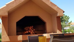 Zona de barbacoa al aire libre con horno de ladrillo, mesa y sillas de madera.