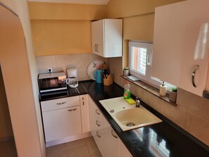 A compact kitchen with white cabinets, a black countertop, a coffee maker, a sink, and a window with a view.