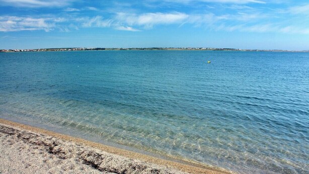 Una vista despejada de una playa con aguas tranquilas y una costa lejana.