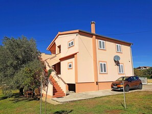 A two-story building with a staircase leading to the entrance, a satellite dish, and a parked car.