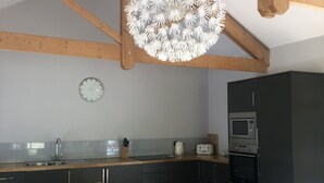 A kitchen with wooden beams, a hanging light fixture, a clock, and modern appliances.
