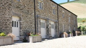 A stone building with multiple doors and windows, surrounded by gravel and plants. - Daisy Barn - Beautiful Grade 2 listed conversion (Mevagissey)