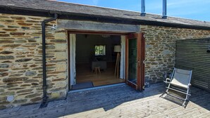 A stone building with a wooden deck, a glass door entrance, and a metal chair outside. - Daisy Barn - Beautiful Grade 2 listed conversion (Mevagissey)