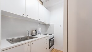 Une cuisine compacte avec des meubles blancs, un évier en acier inoxydable, une machine à café et une cuisinière.