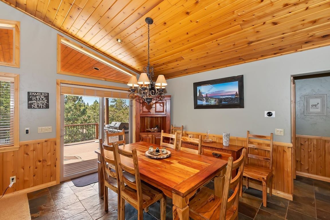 Un coin repas avec une table et des chaises en bois, un lustre et une vue à travers la porte vitrée.
