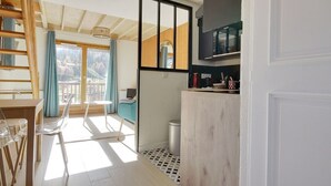 A modern kitchen with a wooden counter, a microwave, and a sink. There is a dining area with a table and chairs, and a view of the outdoors through a large window.