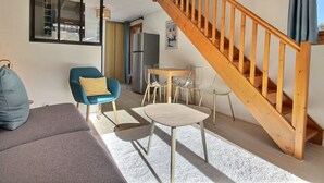 A modern living room with a wooden staircase, a blue armchair, a small round table, and a refrigerator.