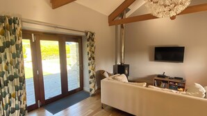 A spacious living room with wooden flooring, a white sofa, a flat-screen TV, and a ceiling fan. - Blossom Barn - Beautiful Grade 2 listed barn conversion (Mevagissey)
