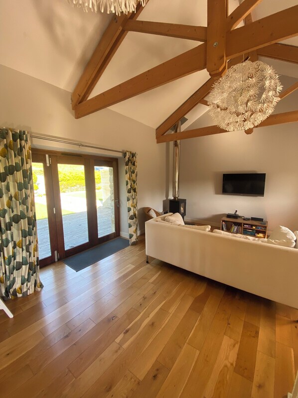 A spacious living room with wooden flooring, a white sofa, a flat-screen TV, and a ceiling fan.