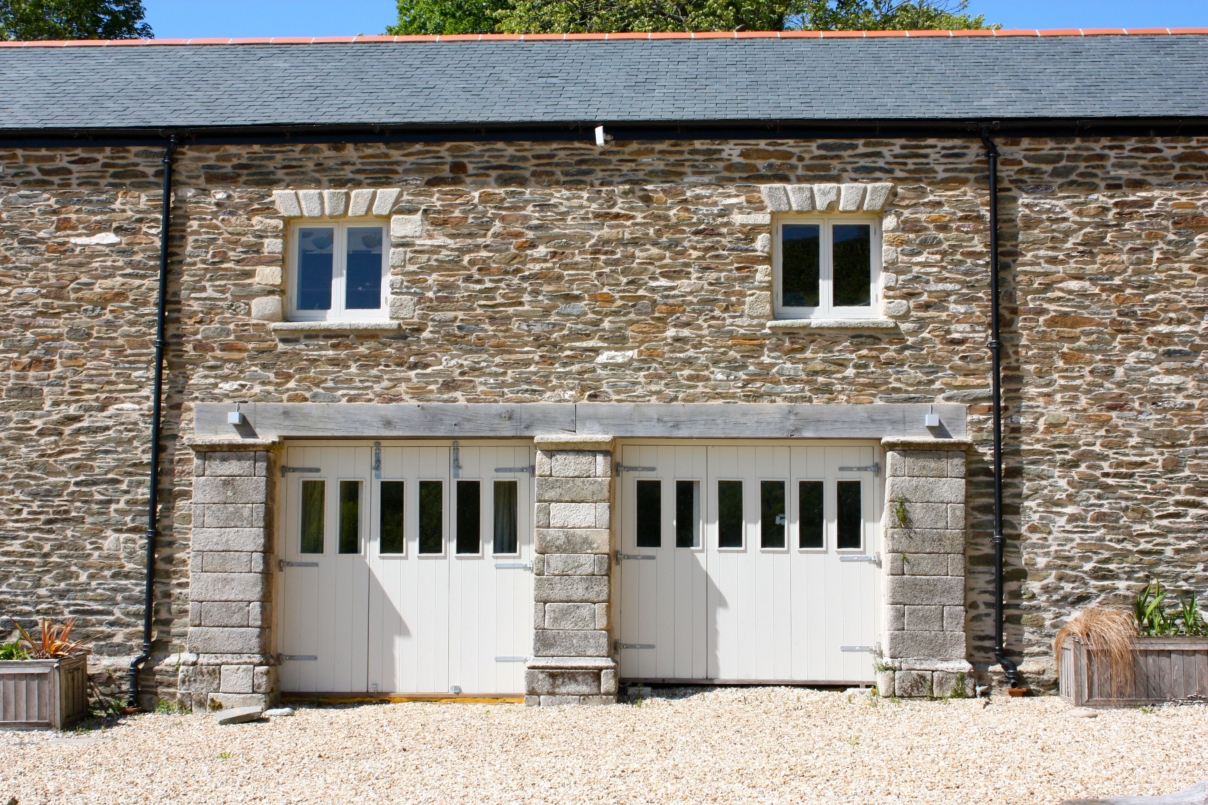 Un bâtiment en pierre avec deux portes blanches et deux fenêtres.