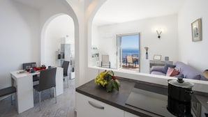A modern kitchen with a dining area, a view of the sea, and a living area with a sofa and a coffee machine.