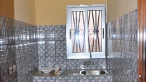 A compact kitchen with a tiled backsplash, a window with decorative bars, a sink, and wooden cabinets.