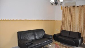 A living room with two black leather sofas, a glass coffee table, a chandelier, and a curtain.