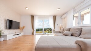 Una sala de estar moderna con un sofá grande, un televisor de pantalla plana y vistas a un jardín a través de amplios ventanales.