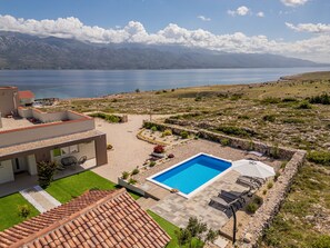 Une maison moderne dotée d’une piscine, d’un patio et offrant une vue sur la mer et les montagnes.