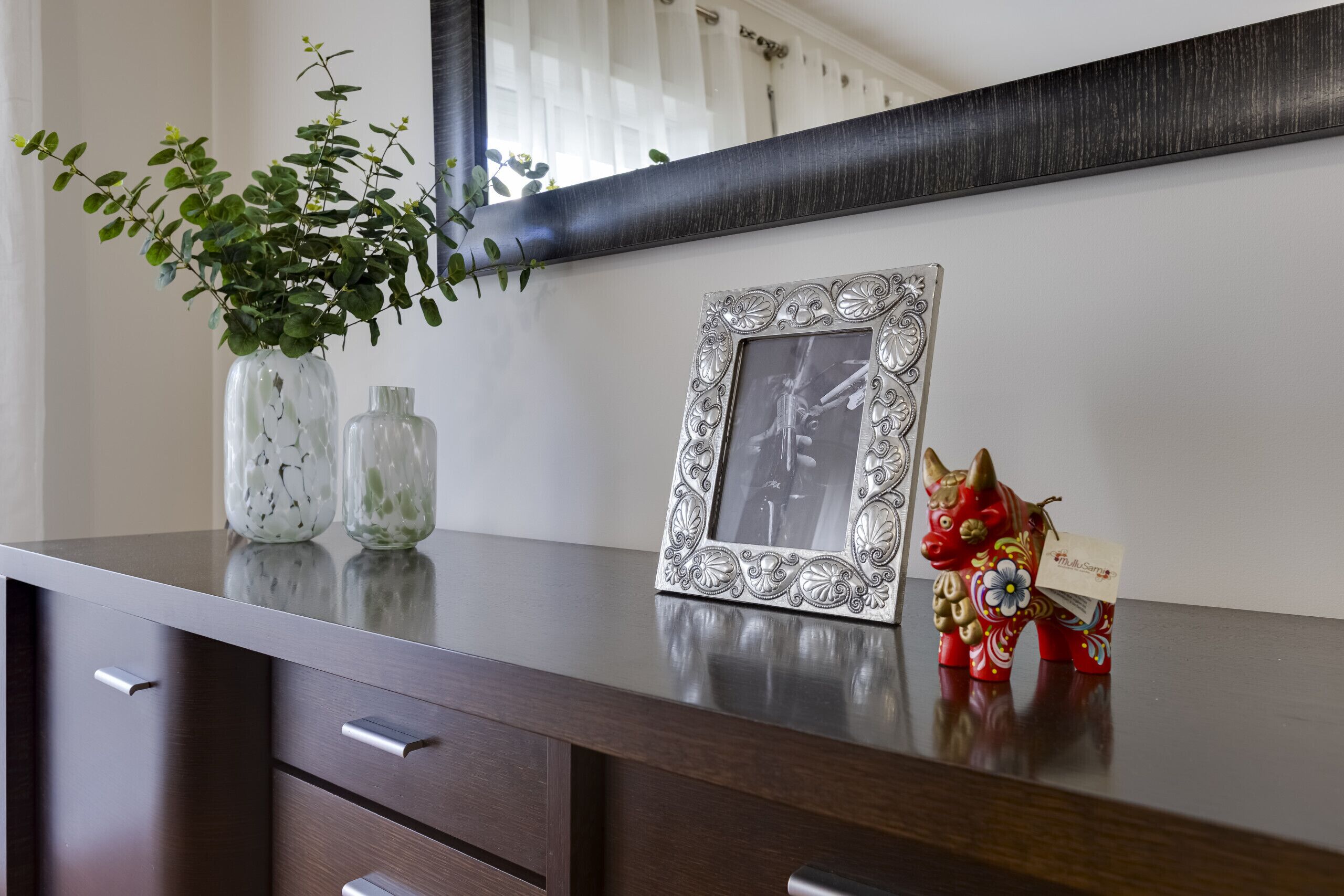 A wooden dresser with a mirror, a decorative picture frame, and a small red figurine.