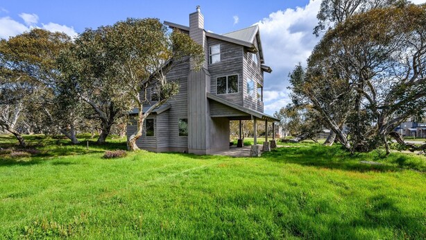 Une maison à deux étages dotée d’un porche abrité, entourée d’une pelouse verdoyante et d’arbres.