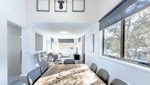 Un espace de restauration moderne avec une longue table, des chaises et une vue sur les arbres à travers de grandes fenêtres.