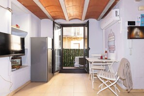 A compact kitchen with a refrigerator, a flat-screen TV, and a dining area with a table and chairs.