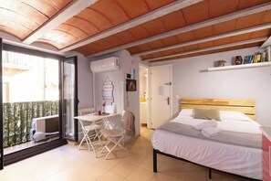 Un dormitorio con cama, una mesa y una silla, un balcón con vistas, y una puerta que da a un baño.