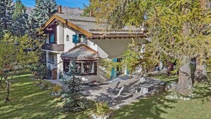 Ein zweigeschossiges Haus mit einer Steinterrasse, einem kleinen Gazebo und einem großen Baum im Vordergrund.
