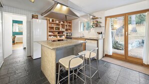 Eine moderne Küche mit einer zentralen Kochinsel, Barhocker und Ausblick ins Freie durch eine Schiebetür.