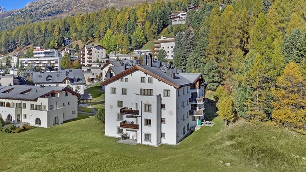 A residential area with modern buildings, a prominent mountain in the background, and a dense forest. - Beautiful 2-room apartment on the raised ground floor with approx. (Champfèr)
