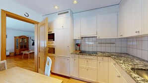 A modern kitchen with white cabinets, a granite countertop, and stainless steel appliances. - Beautiful 2-room apartment on the raised ground floor with approx. (Champfèr)