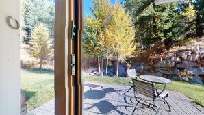 A patio with a table and chairs, a stone wall, and trees in the background. - Beautiful 2-room apartment on the raised ground floor with approx. (Champfèr)