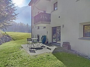 Een gebouw met twee verdiepingen, een balkon, een terras met tuinmeubilair en uitzicht op een bergketen.