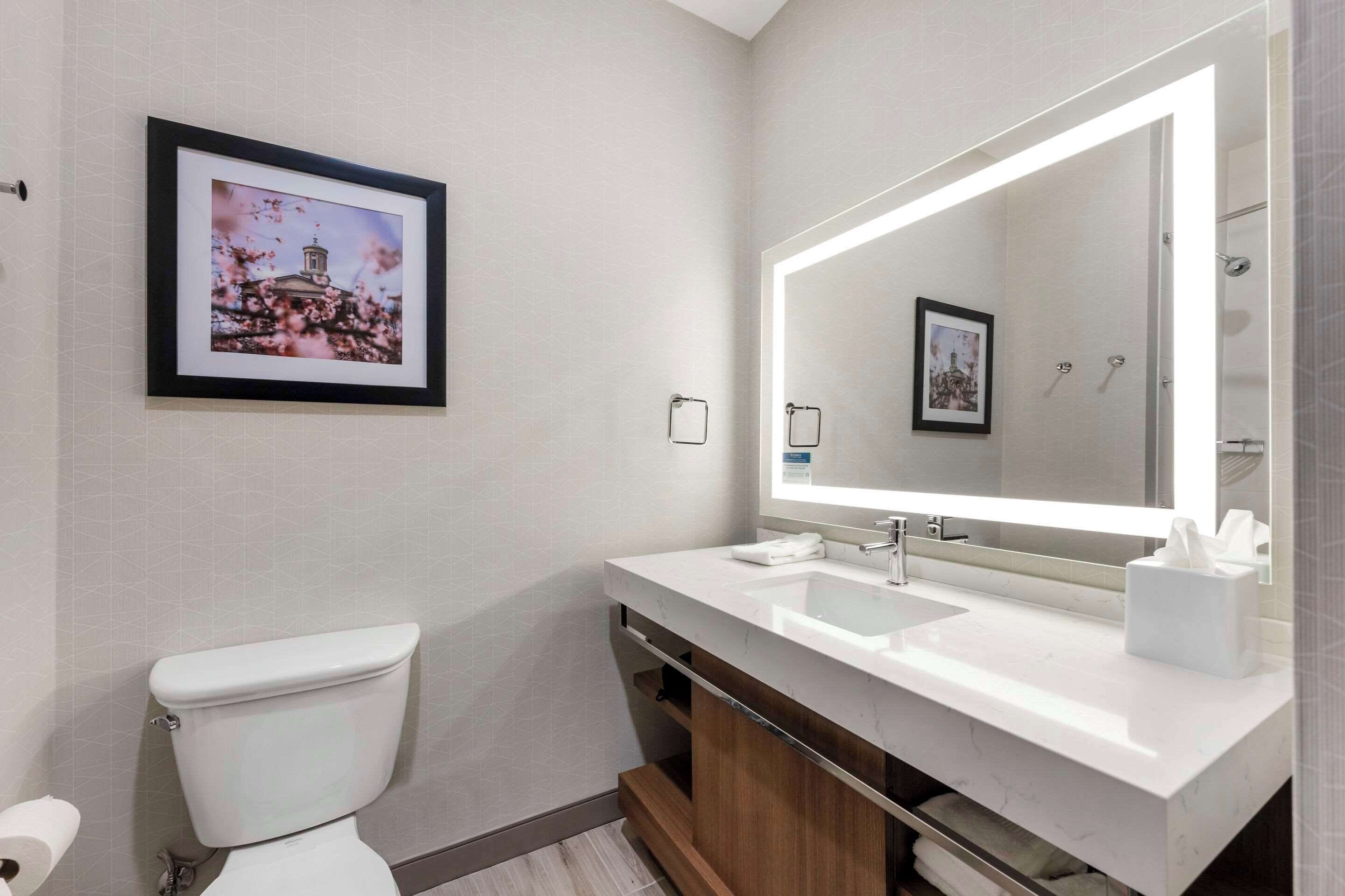 Une salle de bain moderne avec des toilettes blanches, un grand miroir et un lavabo blanc.