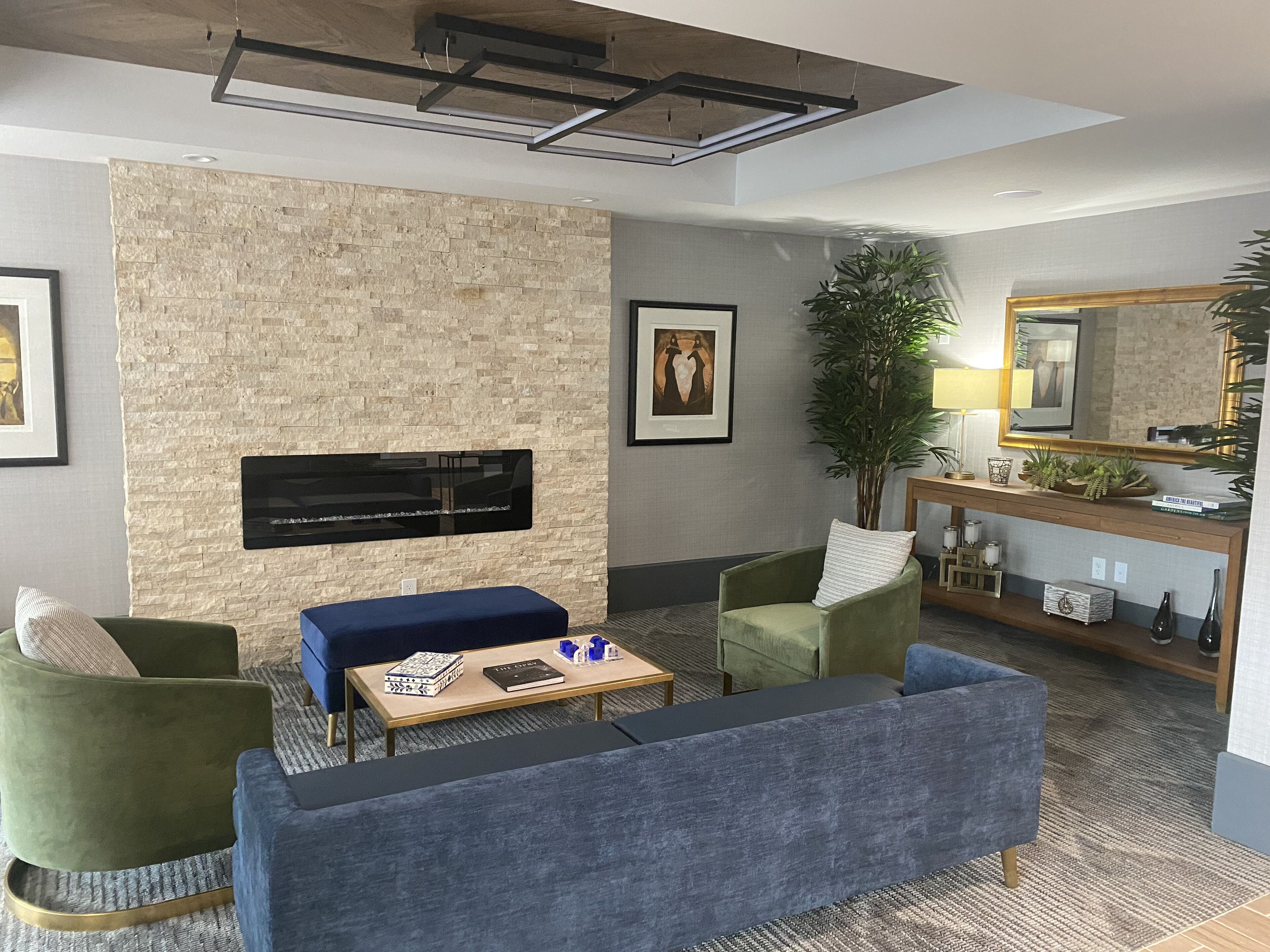 A modern living room with a stone accent wall, a flat-screen TV, a sofa, armchairs, a coffee table, and a console table with decorative items.