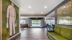 Een ruime lobby met een groene bank, een groot abstract schilderij en uitzicht door de glazen deuren.