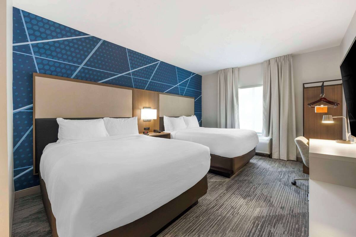 A hotel room with two beds, a desk, and a chair.