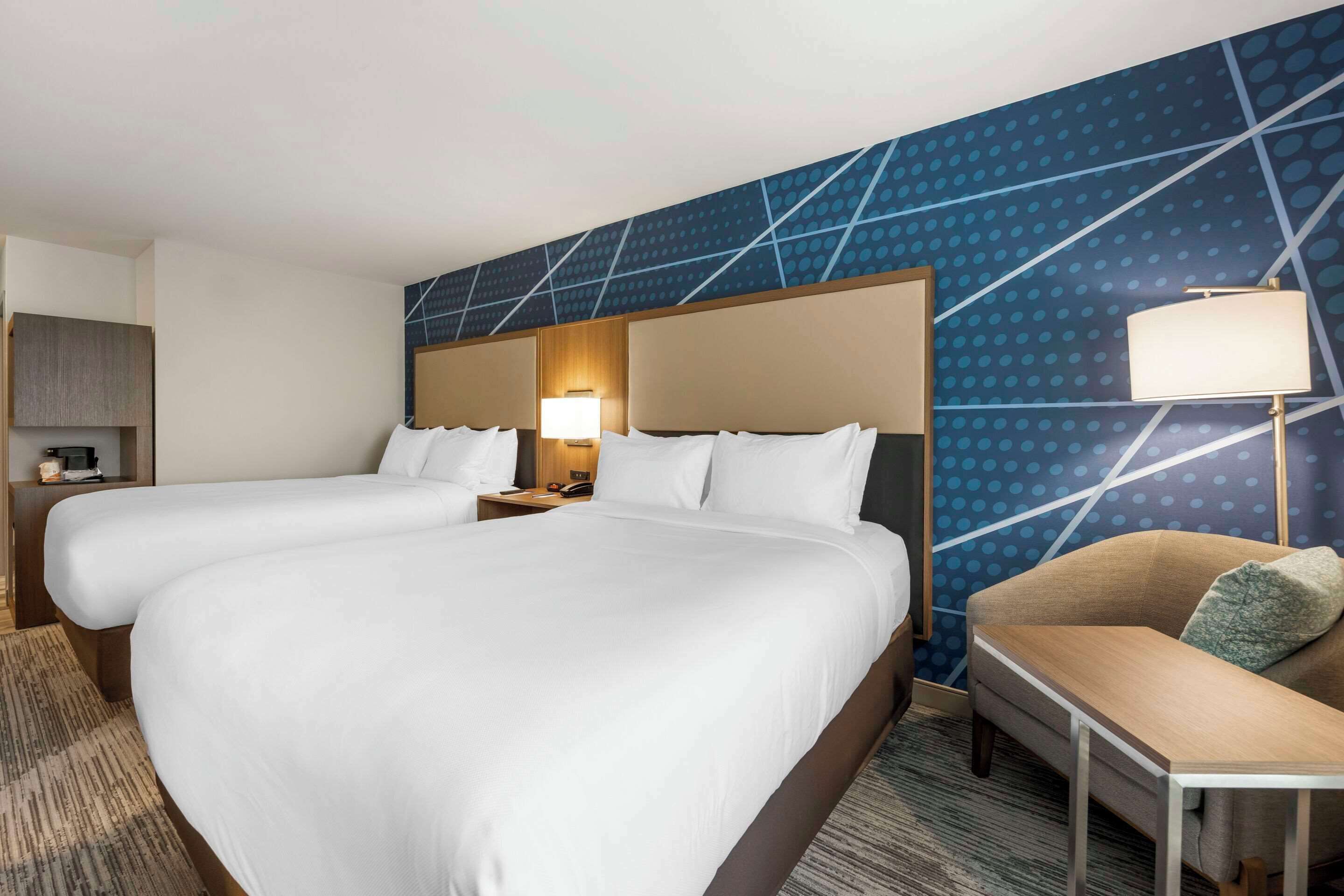 Habitación de hotel con dos camas, un sofá, una lámpara y una pared con diseño geométrico.