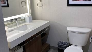 A modern bathroom with a large mirror, two sinks, a toilet, and a trash bin.