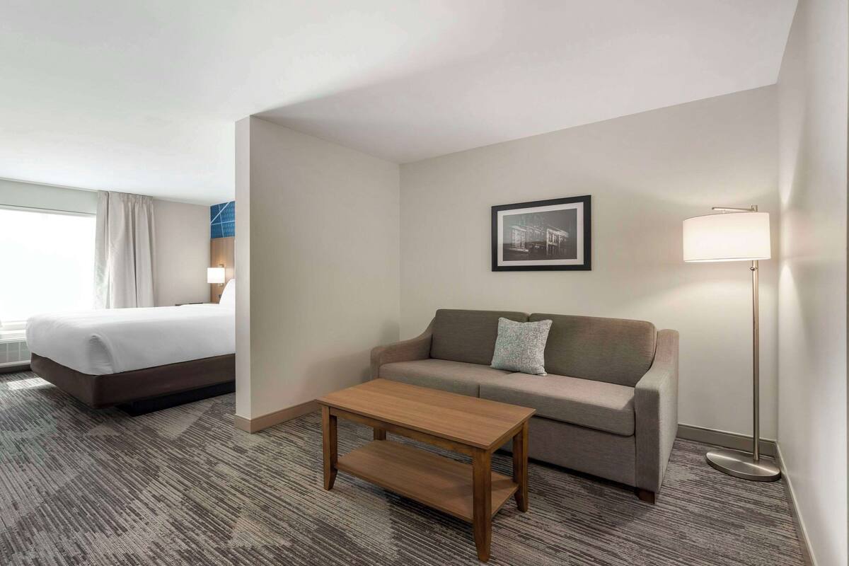 A hotel room with a bed, a sofa, a coffee table, a lamp, and a framed picture on the wall.
