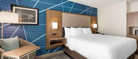 A hotel room with a large bed, a desk, and a chair. There is a wall-mounted picture and two bedside lamps.