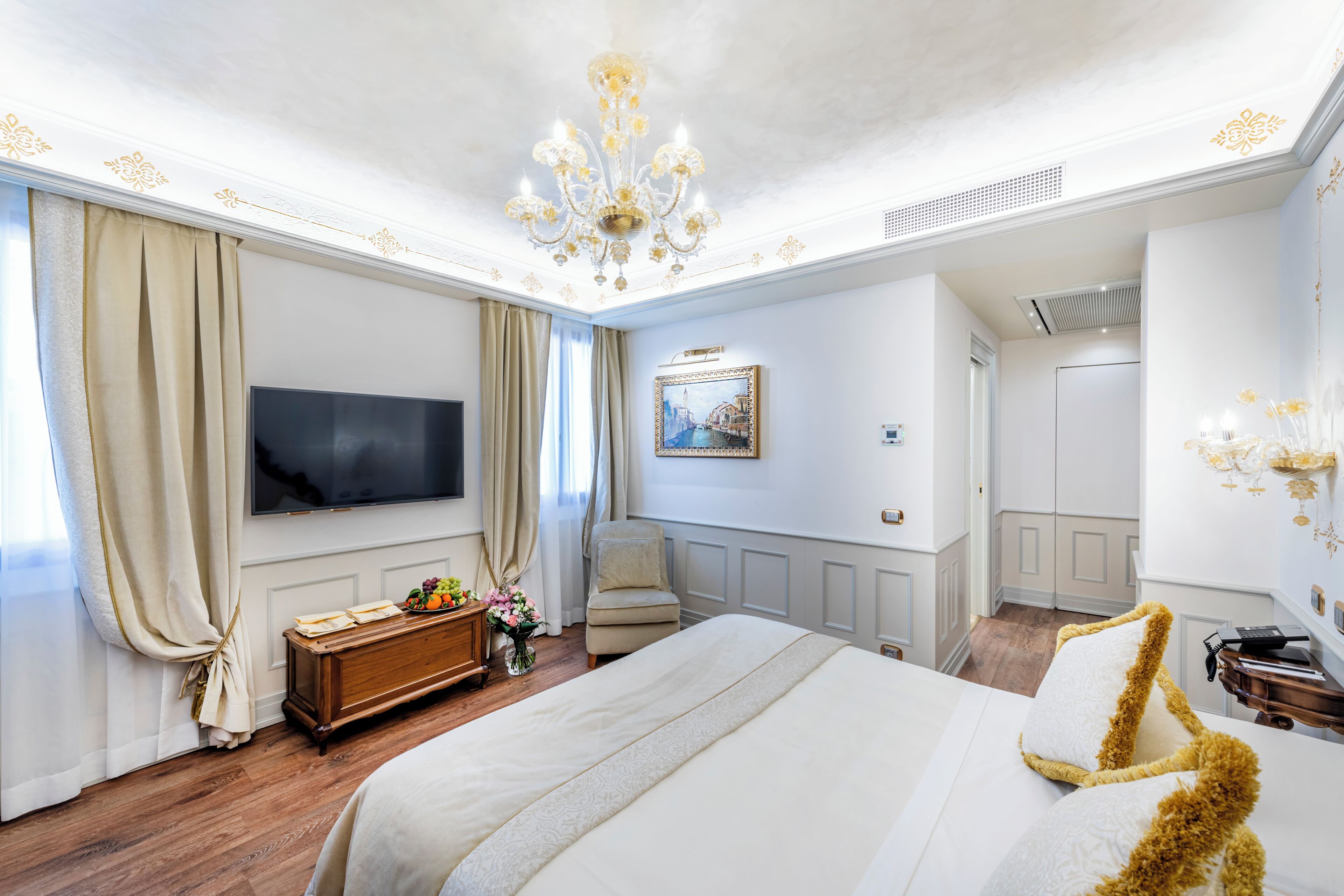 A hotel room with a large bed, a television, a wooden dresser, a chair, and a chandelier.