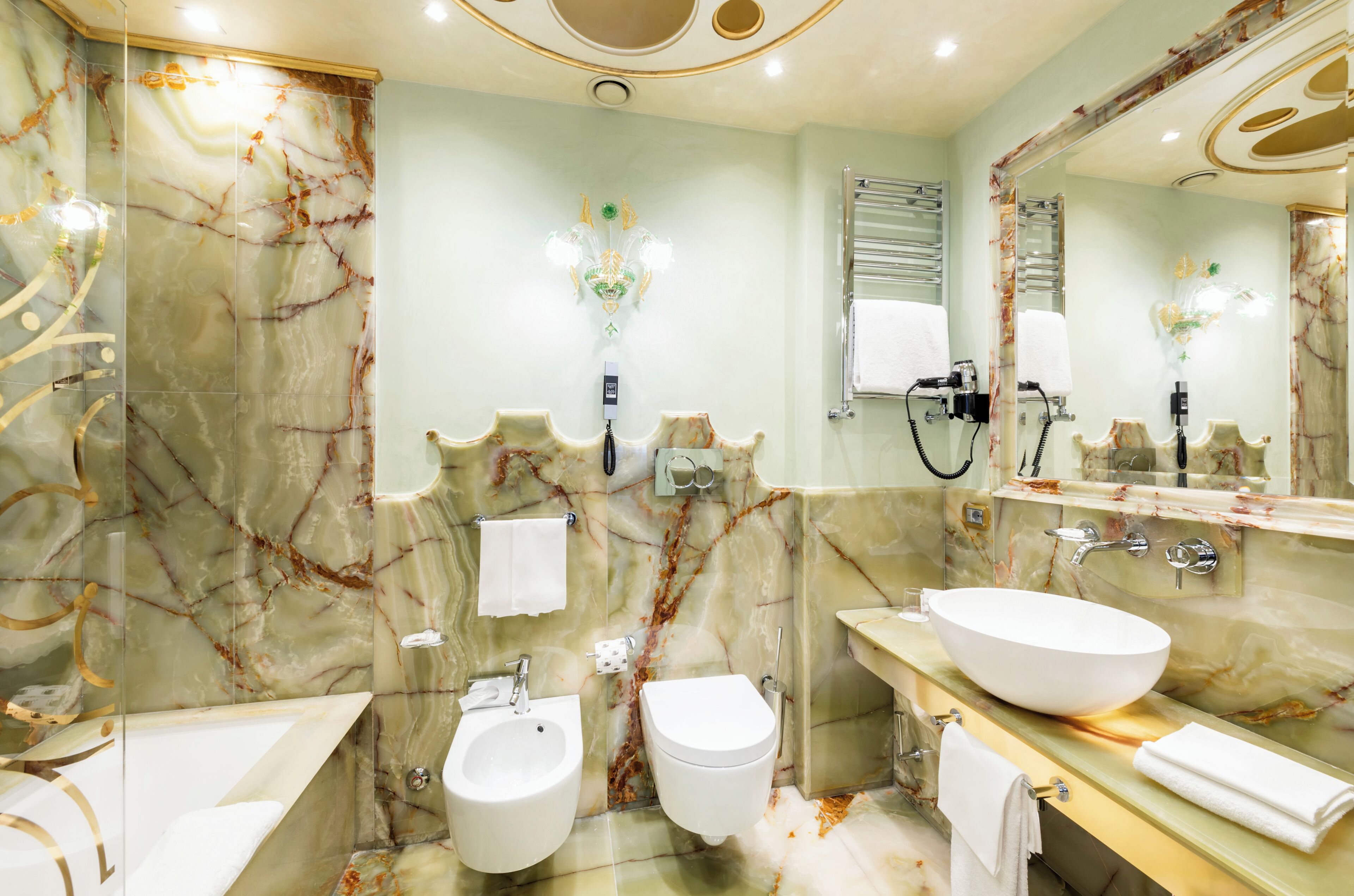 Une salle de bain avec un mur en marbre, un grand lavabo, un bidet et un miroir.