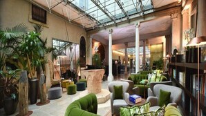 Un hall espacioso con techos altos, ventanas amplias y una zona de estar central con sofás verdes.