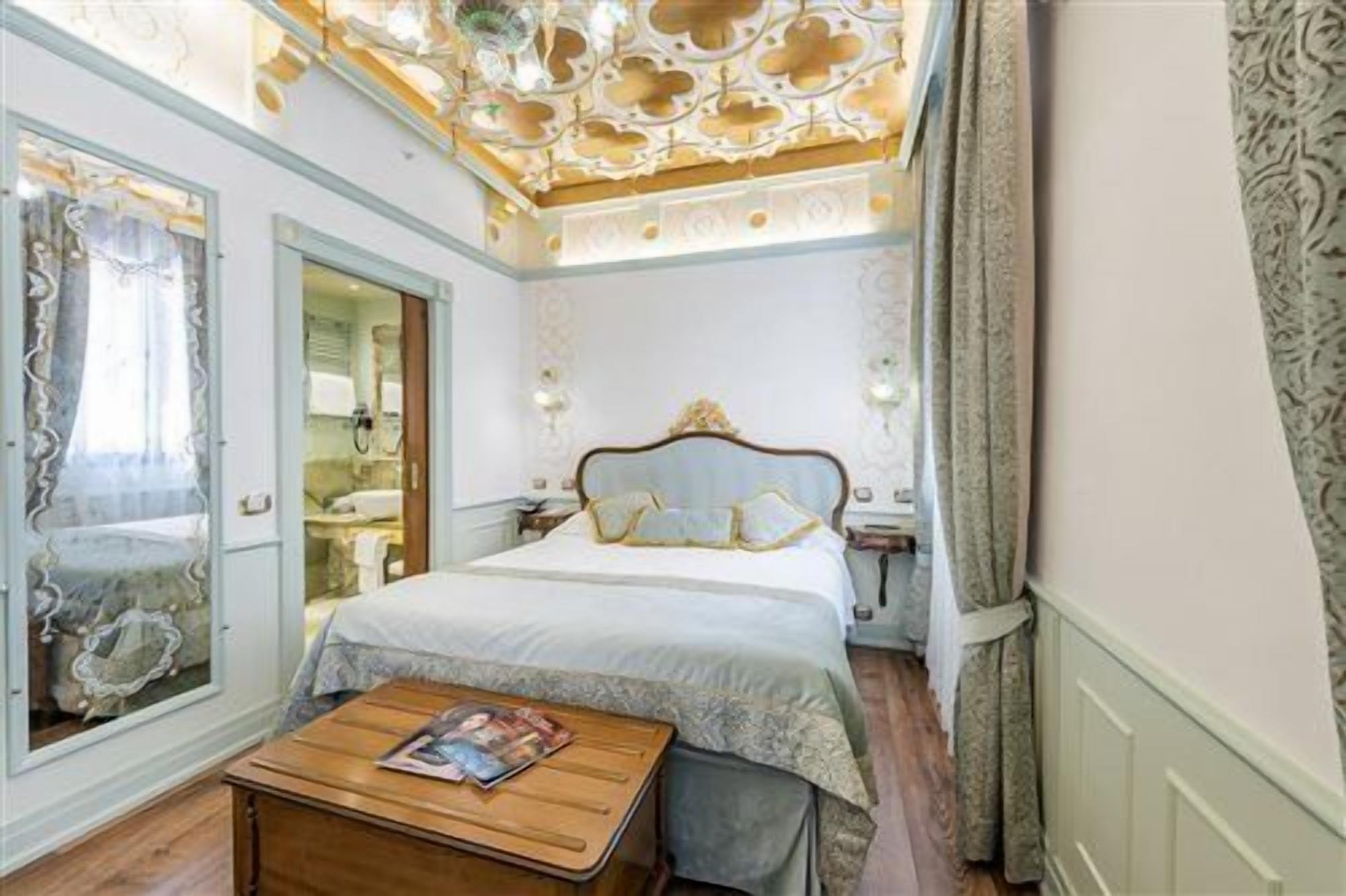 Een hotelkamer met een bed, een houten nachtkastje, een spiegel en een raam met gordijnen.