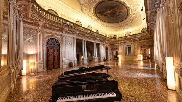 Un salón majestuoso con un piano de cola, columnas ornamentadas y un techo alto con un fresco.