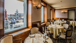 Un restaurante con mesas dispuestas para comer, amplios ventanales que ofrecen vistas a un paisaje urbano y una araña en la pared.