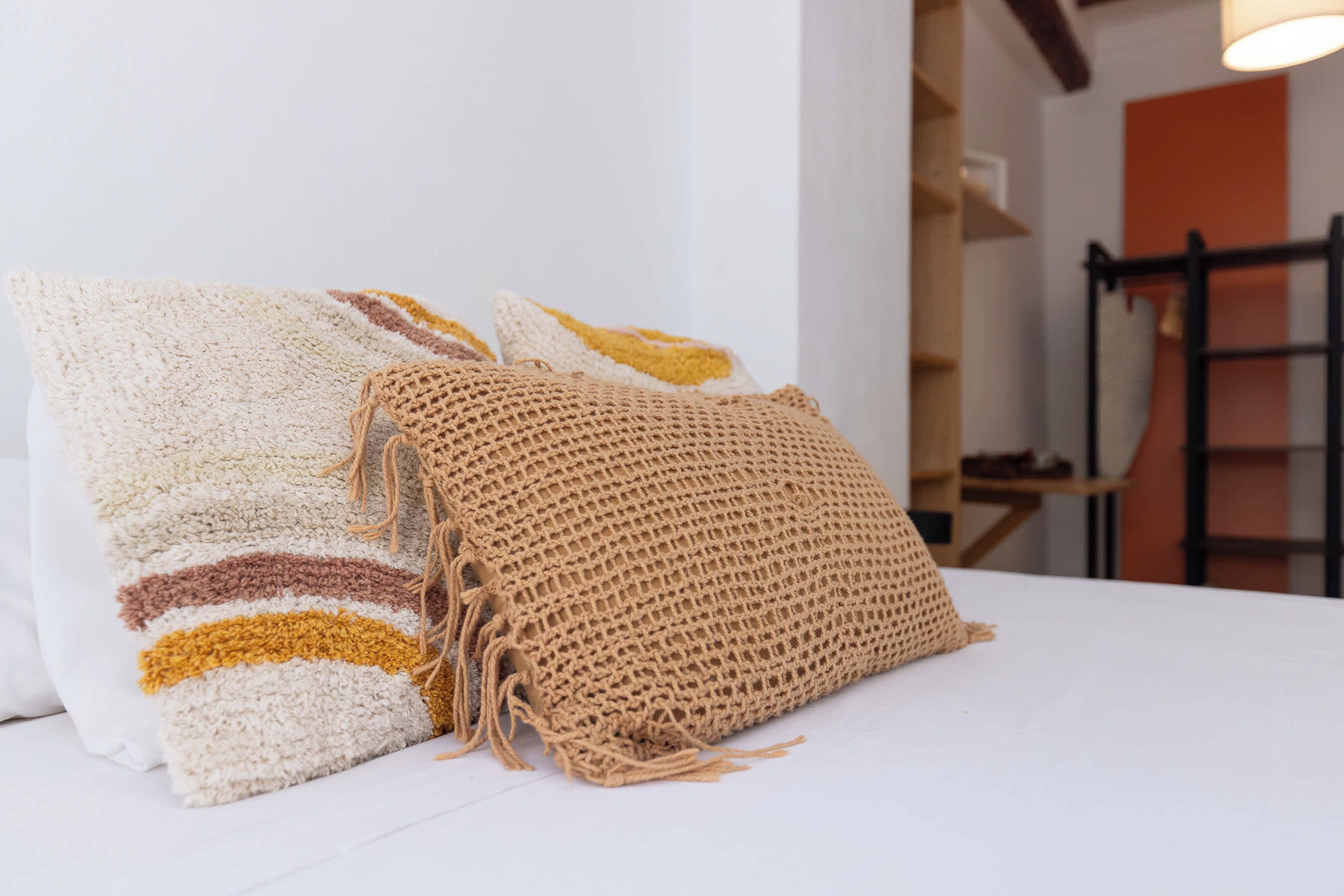 Una cama con sábana blanca y dos almohadas decorativas.
