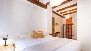 A bedroom with a large bed, wooden beams, a nightstand, and a shelf with books and a lamp. - Catedral - Unik Vacation (Tarragona)