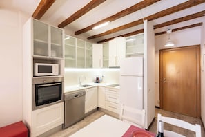 A compact kitchen with white cabinets, a microwave, an oven, a dishwasher, and a wooden door.