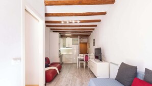A compact room with a bed, a desk, a chair, and a kitchenette in the background. - Catedral - Unik Vacation (Tarragona)