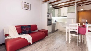A red sofa with a white throw blanket, a wooden ceiling, a kitchen with white cabinets, and a dining table with chairs. - Catedral - Unik Vacation (Tarragona)